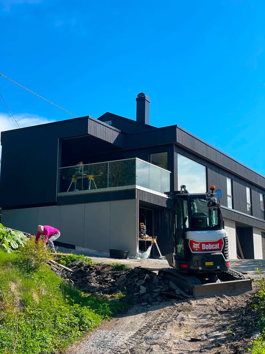 Moderne svart enebolig med glassrekkverk under oppføring
